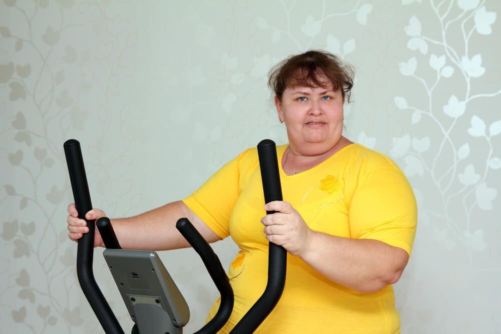 An overweight woman exercises on a stationary trainer.