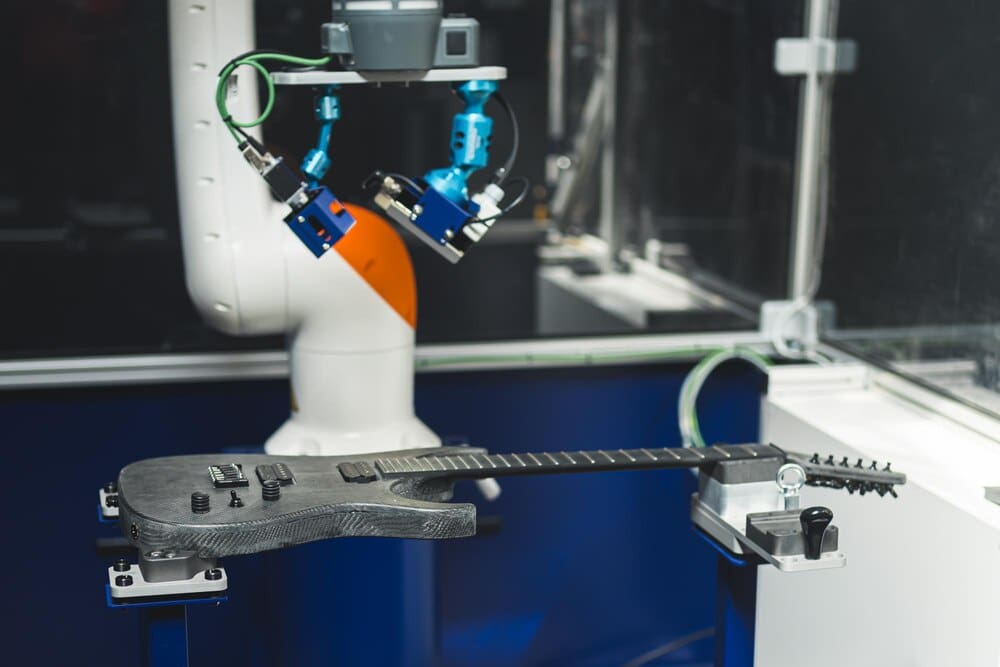 A robotic arm uses a paint control system to check the quality of a gray guitar.