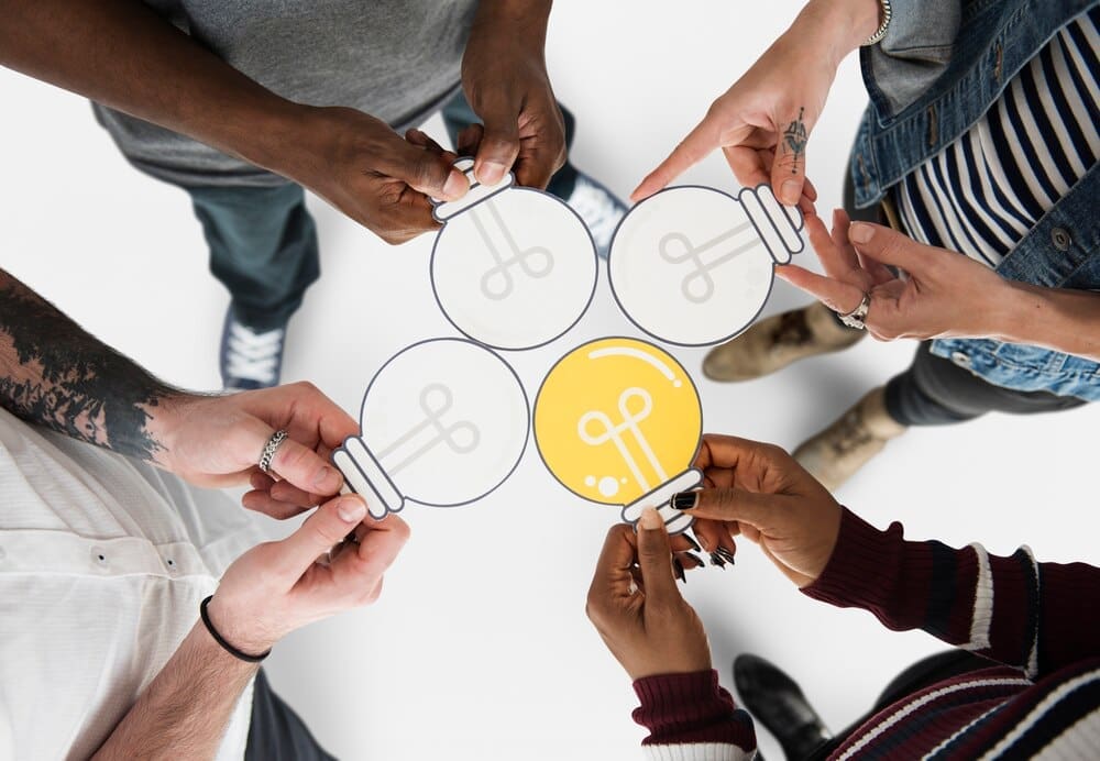 People holding a paper cutout of a light bulb icon.
