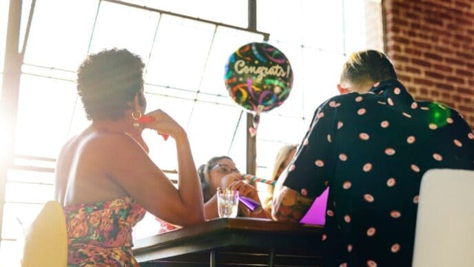 People of varying ages are gathered at a party, joyfully interacting with colorful balloons.