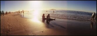 People of various ages stand and sit on a sandy beach.