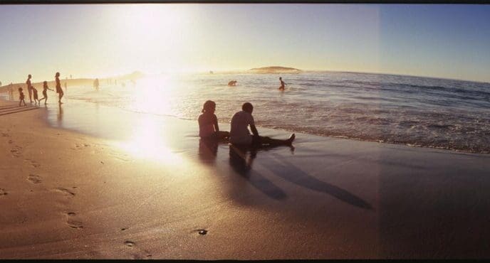 People of various ages stand and sit on a sandy beach.