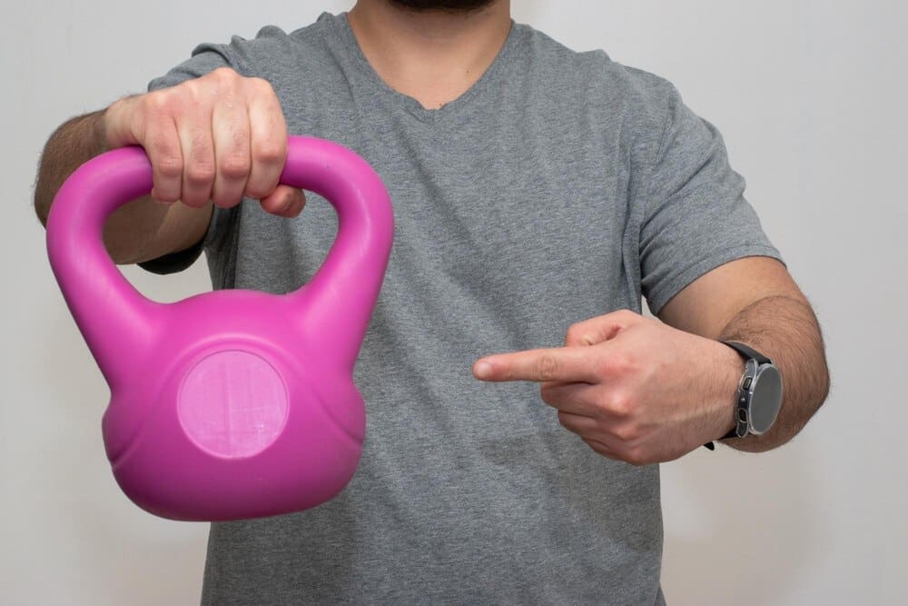 A person holds a pink dumbbell and points their finger.