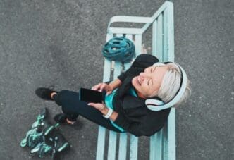 A mature woman wearing roller skates prepares to skate while listening to a podcast on her phone, smiling.