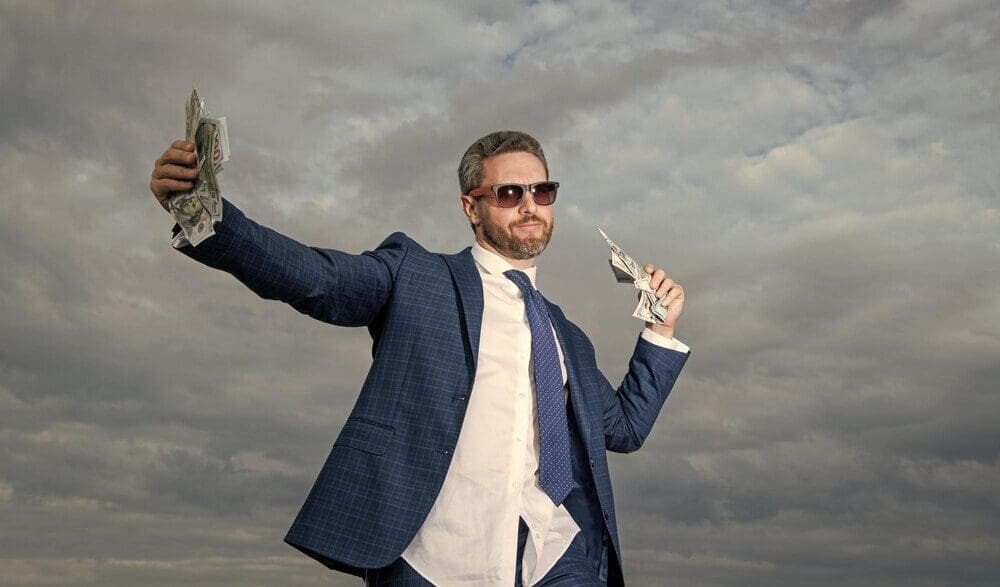 A smiling billionaire man holds money against a blue sky background.