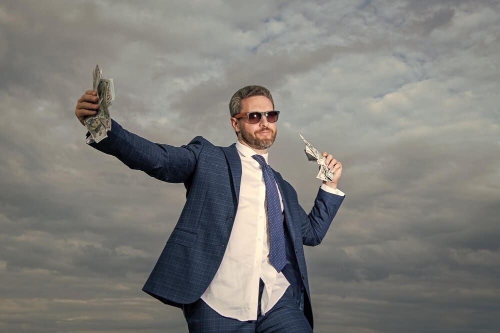 A smiling billionaire man holds money against a blue sky background.
