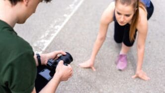 A photographer takes a photo of a young, blonde woman in sportswear, preparing to run on a road during an outdoor training session.