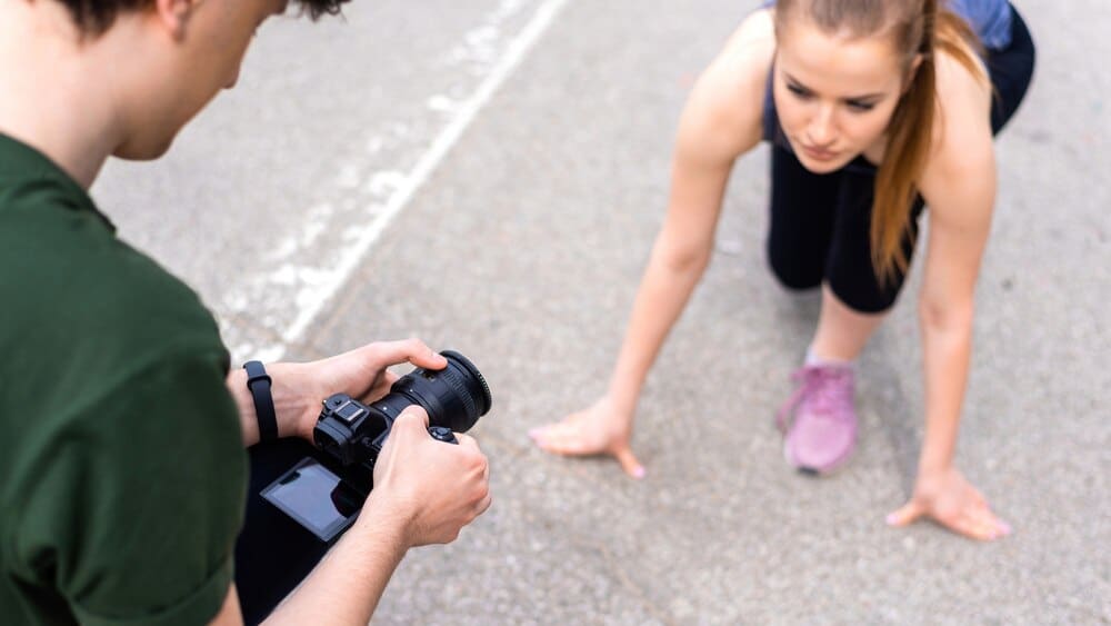 A photographer takes a photo of a young, blonde woman in sportswear, preparing to run on a road during an outdoor training session.
