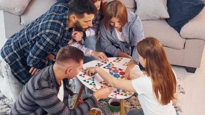 Friends gather indoors, laughing and working together to solve a puzzle.