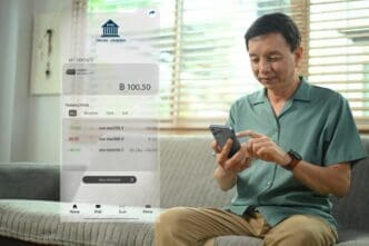An older man smiles while looking at his smartphone, likely checking his banking app or electronic wallet.