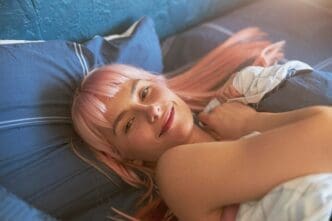 Attractive young woman with pink hair awakens in a large, comfortable bed.