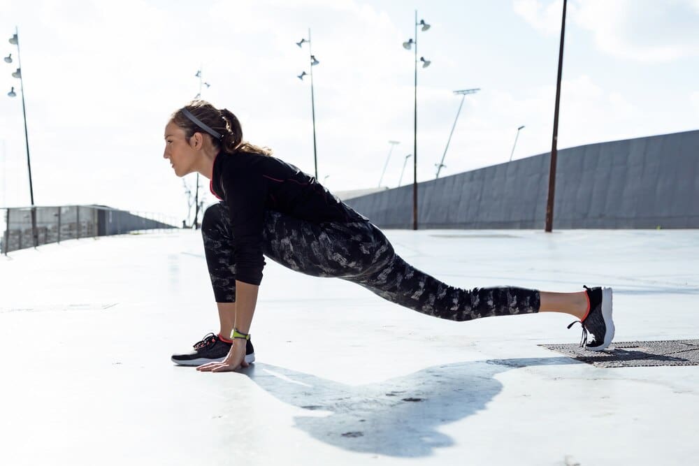 A young woman in athletic wear stretches in an urban setting.