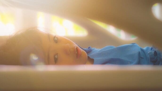 A young girl is lying down on a bed, likely resting or relaxing.