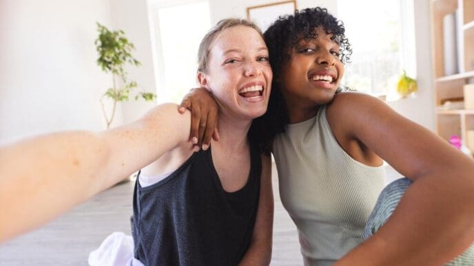 Smiling diverse female friends in athletic wear take a selfie together indoors.