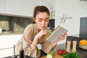 Young woman in a modern kitchen reads a recipe and grocery list while preparing a salad.