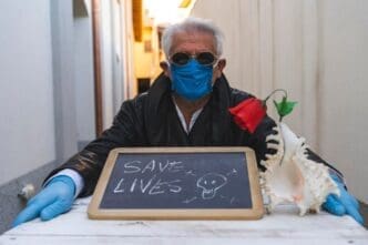A senior man wearing a face mask sits at a table.
