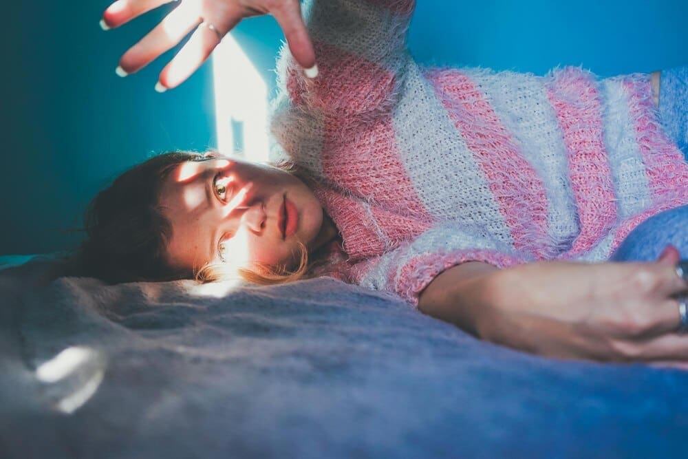 A woman is lying on a bed, likely in a portrait setting.
