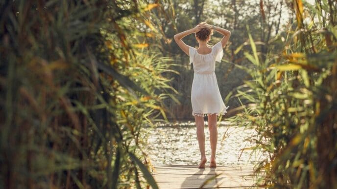 A young girl in a light dress stands among reeds in a retro-style portrait.