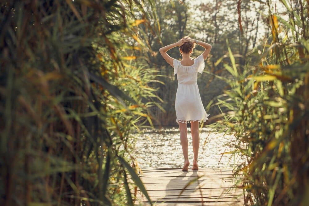A young girl in a light dress stands among reeds in a retro-style portrait.