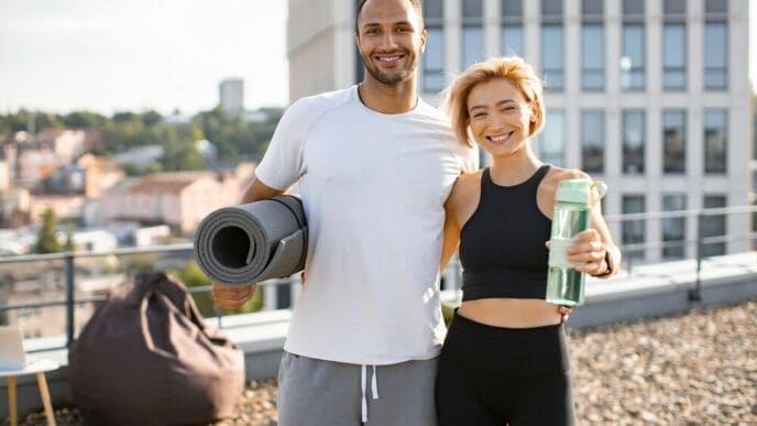 A young couple in athletic wear exercises outdoors in front of a city backdrop.
