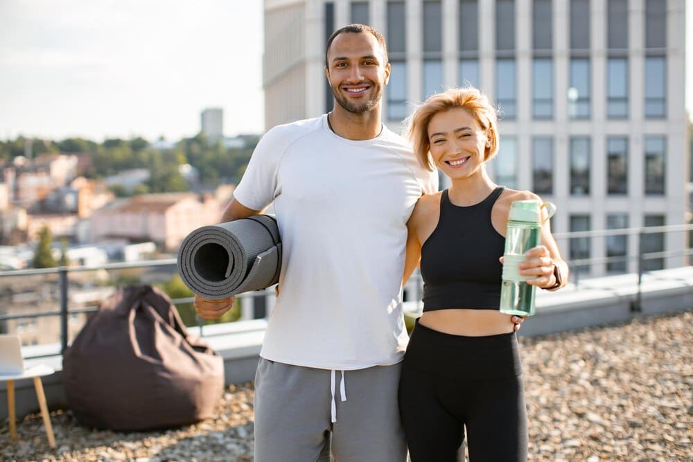 A young couple in athletic wear exercises outdoors in front of a city backdrop.
