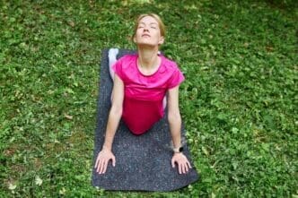 A woman with European features practices yoga on a mat in a park.