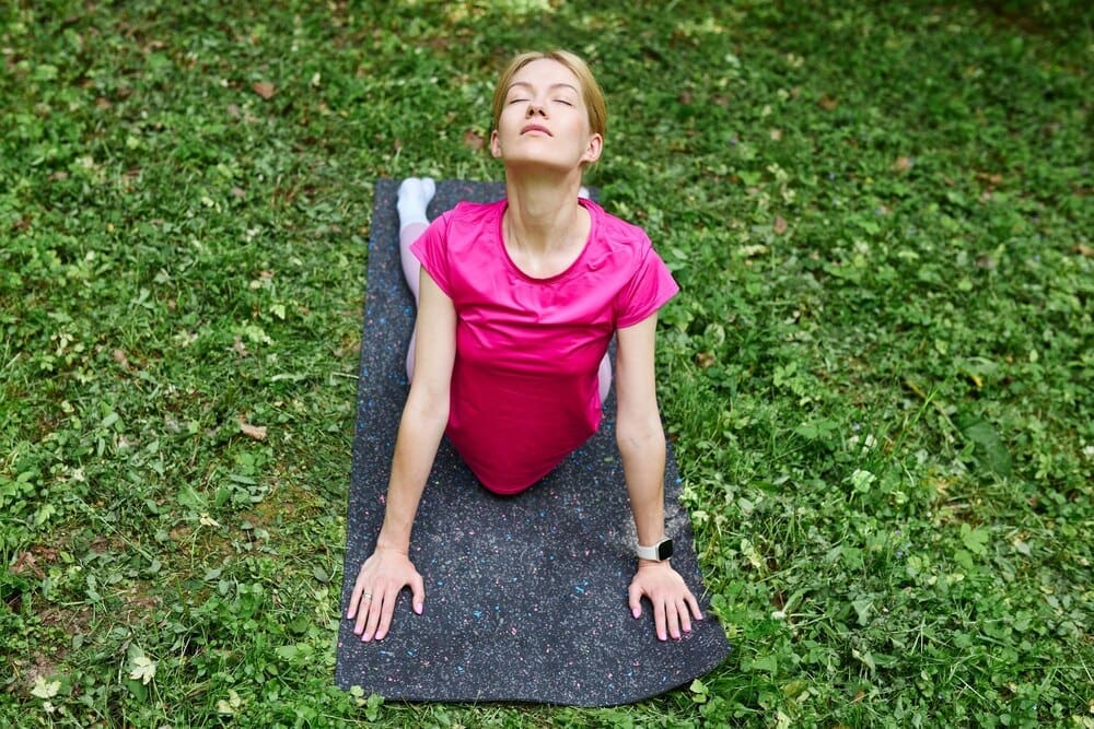 A woman with European features practices yoga on a mat in a park.