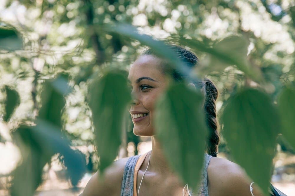 A young woman with long hair and a ponytail takes a break from exercising, resting her hands on her knees.