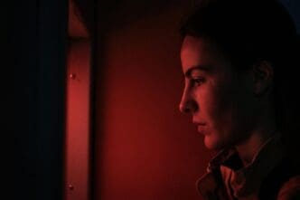 Profile of a young woman standing in a dark room, illuminated by an unseen light source.