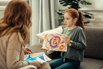 A smiling girl holds a colorful painting and appears to be discussing it.