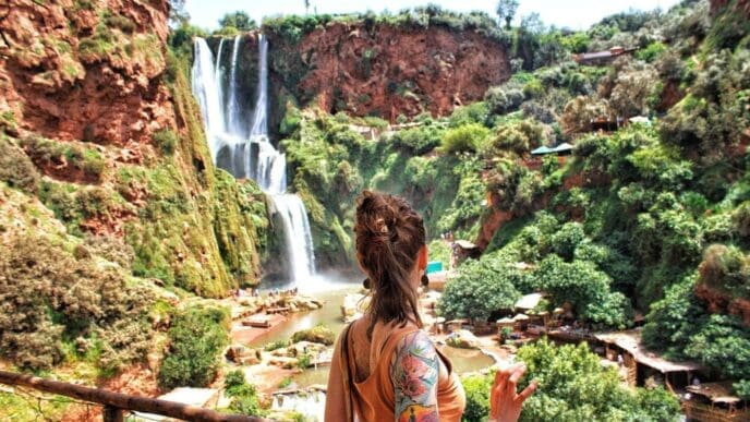 Woman with long hair looking at a waterfall from behind.
