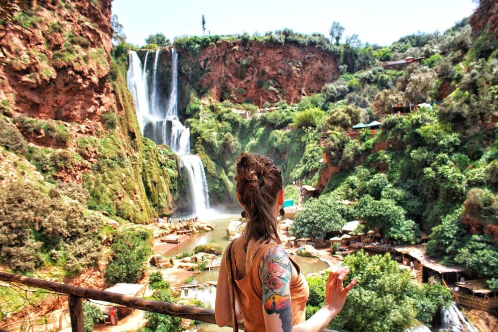Woman with long hair looking at a waterfall from behind.
