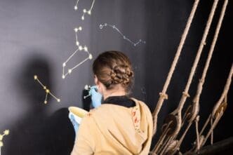 Woman painting star constellations on a chalkboard in a room designed to resemble a ship's deck.