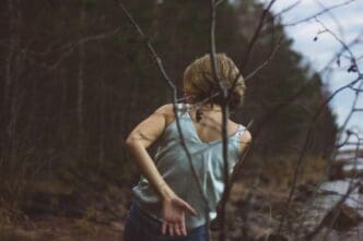 Rear view of a young woman dances in a forest, silhouetted against the trees.