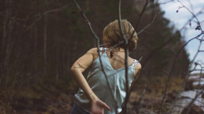 Rear view of a young woman dances in a forest, silhouetted against the trees.