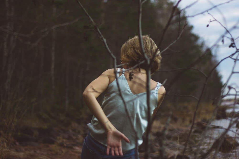 Rear view of a young woman dances in a forest, silhouetted against the trees.