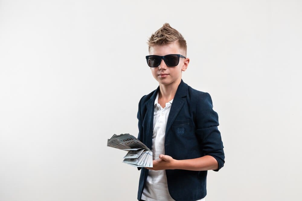 A young person with a smug expression holds a large stack of money, implying financial wealth.
