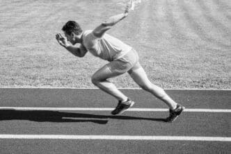 A runner bursts forward from the starting position on a stadium track on a sunny day, illustrating the beginning of a sprint race.