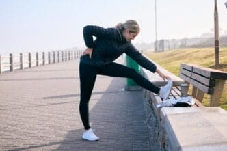 A woman stretches her legs on a beach, preparing for a morning run with the ocean in the background.
