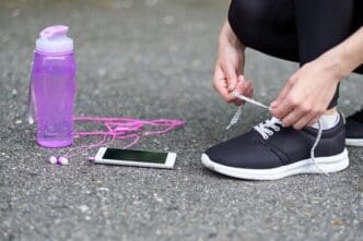 Woman tying running shoe laces on a track, with a water bottle and phone nearby.