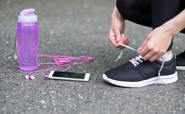 Woman tying running shoe laces on a track, with a water bottle and phone nearby.