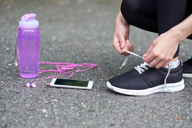 Woman tying running shoe laces on a track, with a water bottle and phone nearby.