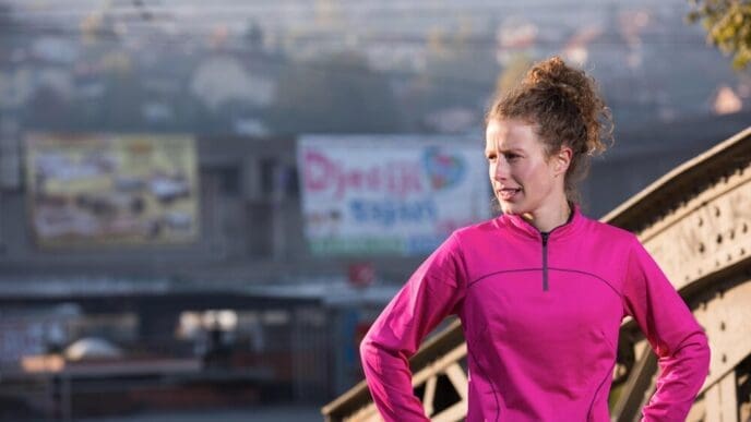 Woman in athletic wear stretches her legs and arms before a morning run.