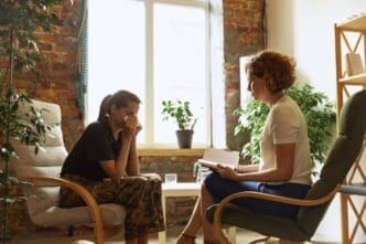 A young man in a military uniform sits with a female psychiatrist in an indoor therapy session.