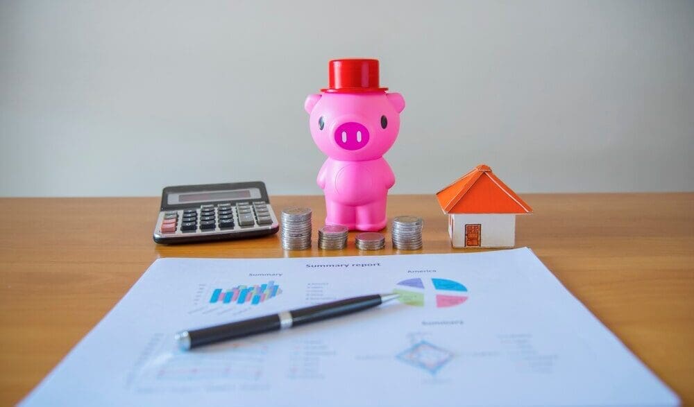 A hand places a coin into a piggy bank, illustrating the concept of saving money.