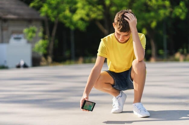 A young boy with a sad expression clutches a broken cell phone while standing in a skatepark.