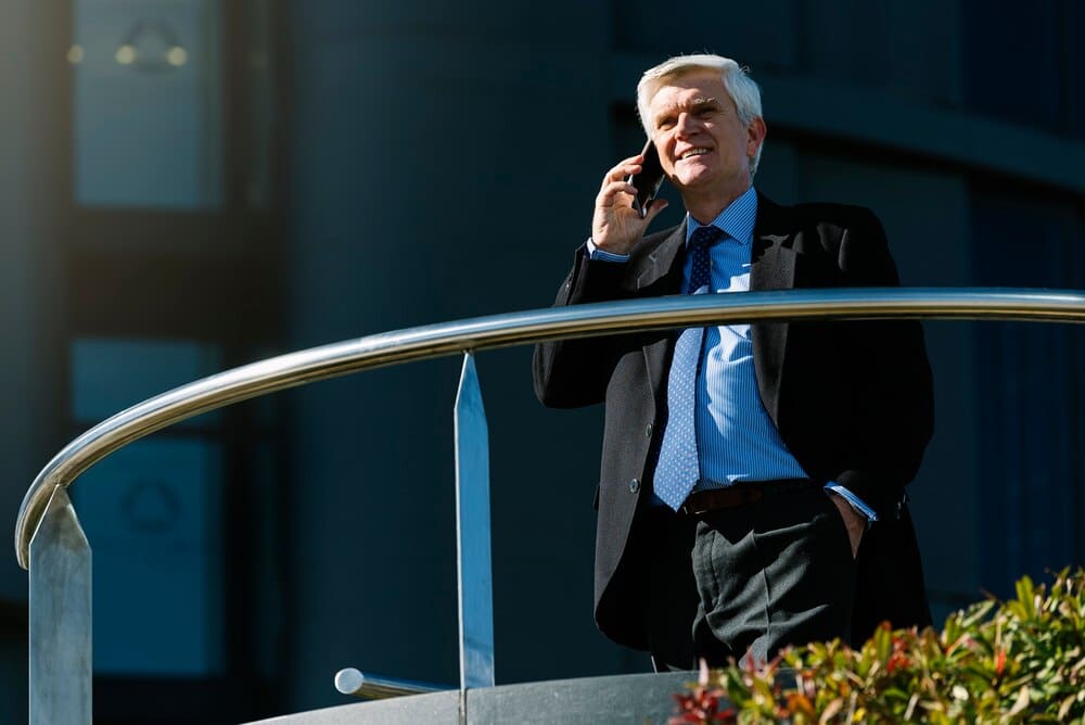 A senior businessman in a suit stands on a city street, possibly representing a business concept.