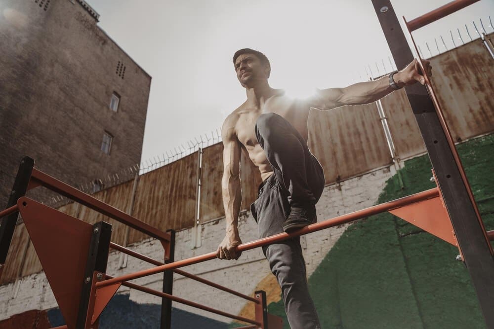 A shirtless athlete with a smartwatch works out outdoors, demonstrating calisthenics.