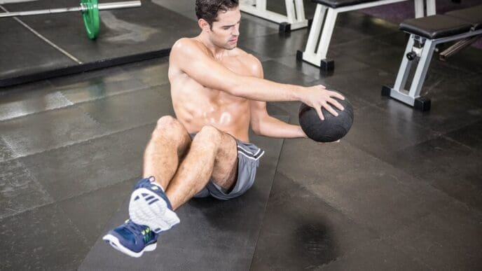 Shirtless man at the gym exercises with a medicine ball.