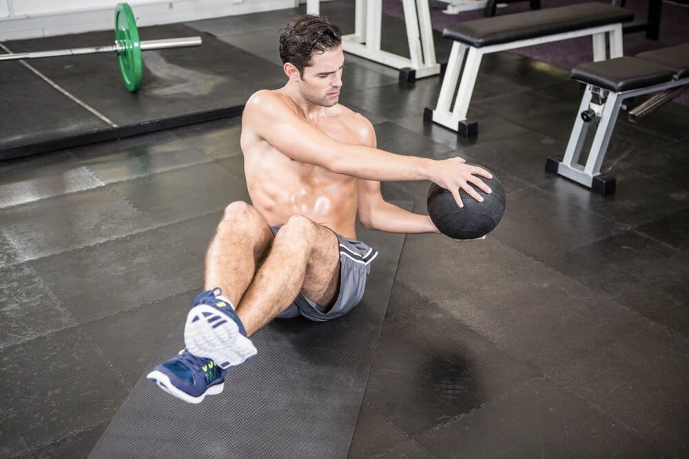 Shirtless man at the gym exercises with a medicine ball.
